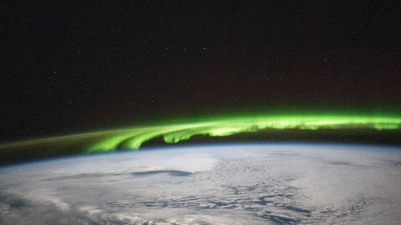 A green aurora arcing above the curve of the Earth, photographed from orbit